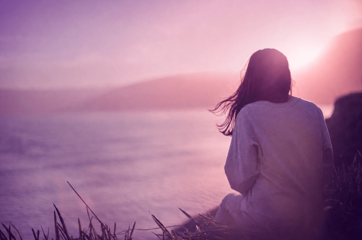 A woman sitting by the water at sunset in a quiet, reflective moment